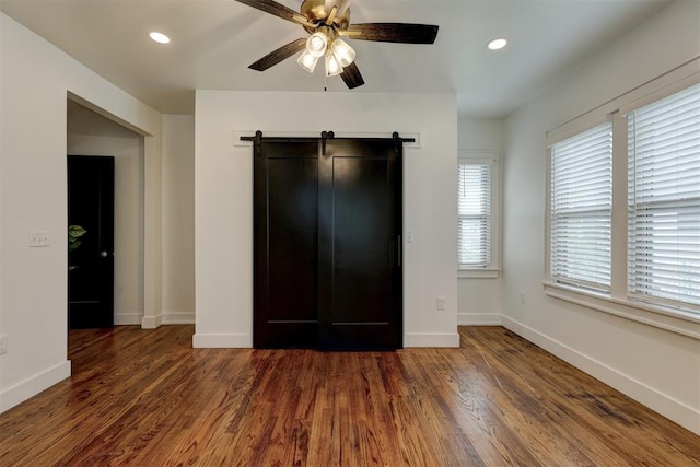 unfurnished bedroom with dark hardwood / wood-style floors, ceiling fan, and a barn door