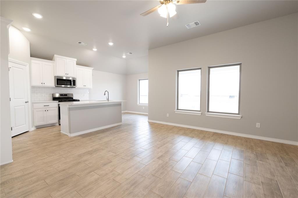 kitchen with an island with sink, ceiling fan, appliances with stainless steel finishes, white cabinets, and sink