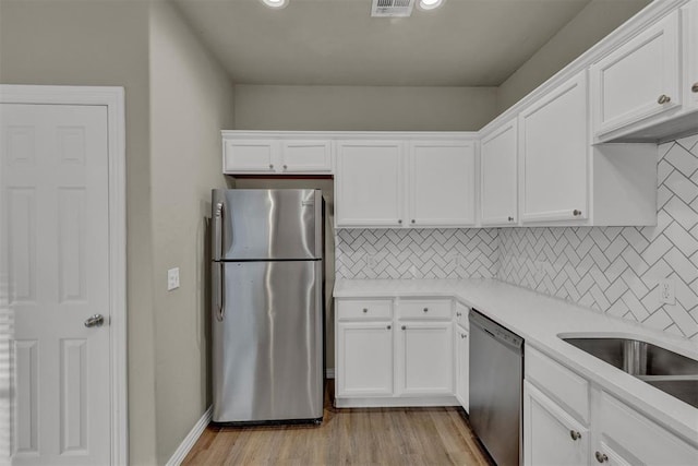 kitchen featuring decorative backsplash, stainless steel appliances, white cabinetry, and light hardwood / wood-style floors