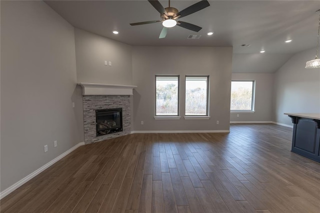 unfurnished living room featuring vaulted ceiling, dark hardwood / wood-style floors, a stone fireplace, and ceiling fan