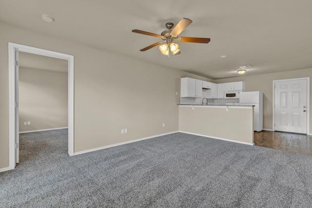 unfurnished living room with dark carpet and ceiling fan