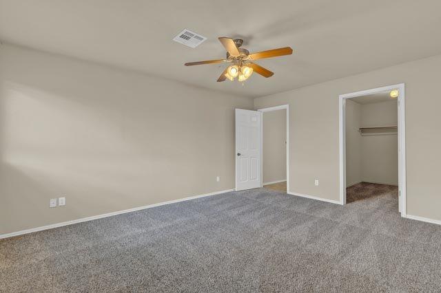 unfurnished bedroom featuring a spacious closet, a closet, ceiling fan, and light carpet