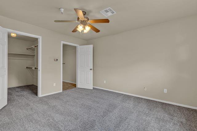 unfurnished bedroom featuring a walk in closet, ceiling fan, a closet, and light colored carpet