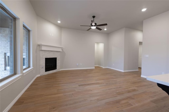 unfurnished living room with ceiling fan, a stone fireplace, and light wood-type flooring