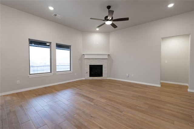 unfurnished living room with ceiling fan, a stone fireplace, and light hardwood / wood-style floors