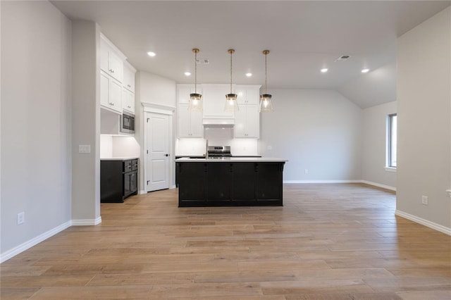 kitchen with light hardwood / wood-style flooring, white cabinetry, a center island with sink, built in microwave, and decorative light fixtures