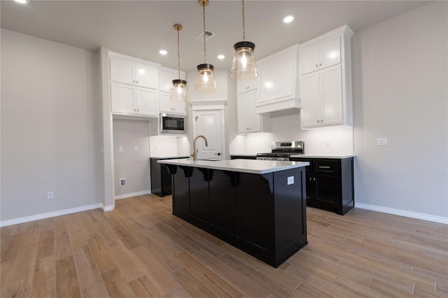 kitchen featuring built in microwave, sink, hanging light fixtures, a kitchen island with sink, and stainless steel range oven