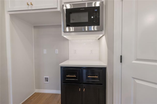 interior details featuring stainless steel microwave, light wood-type flooring, decorative backsplash, and white cabinets