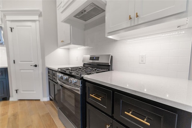 kitchen with tasteful backsplash, white cabinets, light stone countertops, and stainless steel gas range oven