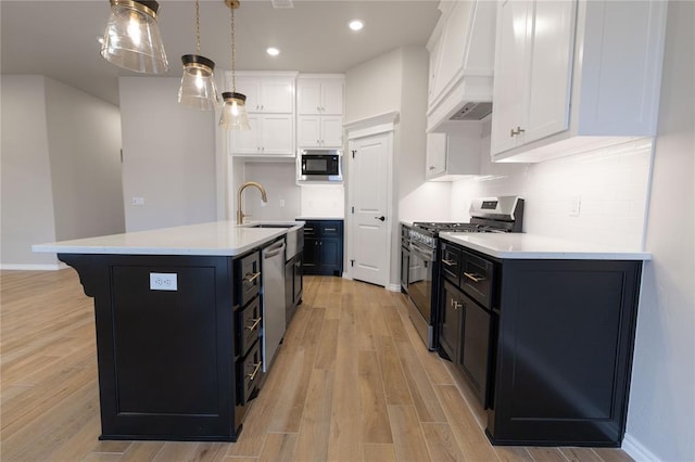 kitchen with stainless steel appliances, hanging light fixtures, a kitchen island with sink, and white cabinets