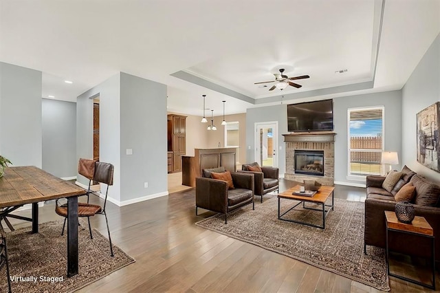 living room featuring ceiling fan, wood-type flooring, and a tray ceiling