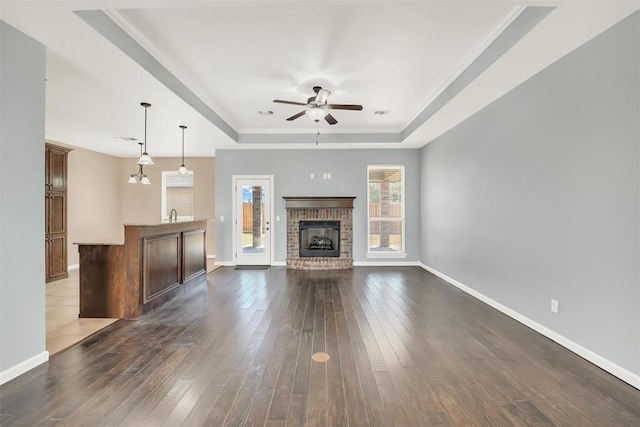 unfurnished living room featuring dark wood-type flooring, ceiling fan with notable chandelier, a raised ceiling, sink, and a brick fireplace