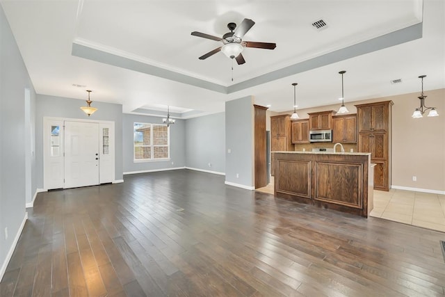 unfurnished living room with a tray ceiling, crown molding, dark hardwood / wood-style flooring, and ceiling fan with notable chandelier