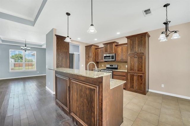 kitchen featuring a tray ceiling, pendant lighting, a chandelier, and appliances with stainless steel finishes