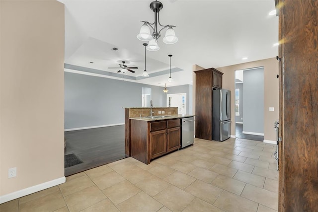 kitchen with light stone countertops, appliances with stainless steel finishes, ceiling fan with notable chandelier, sink, and pendant lighting