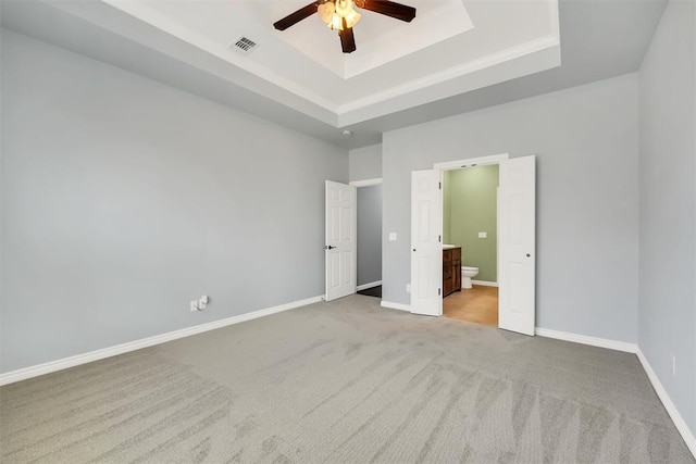 unfurnished bedroom with a raised ceiling, ensuite bathroom, ceiling fan, and light colored carpet