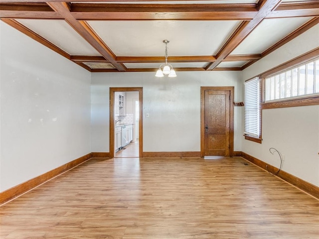 empty room with beamed ceiling, an inviting chandelier, light hardwood / wood-style flooring, and coffered ceiling