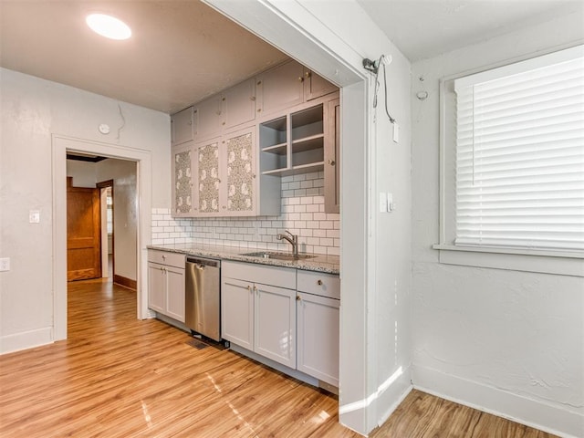 kitchen with light stone countertops, sink, tasteful backsplash, stainless steel dishwasher, and light wood-type flooring