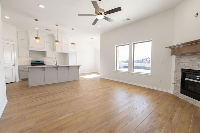 unfurnished living room with ceiling fan, sink, a stone fireplace, and light hardwood / wood-style flooring