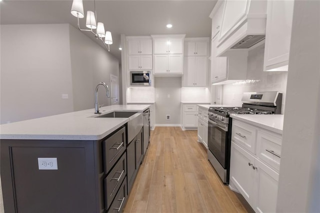 kitchen featuring premium range hood, decorative light fixtures, appliances with stainless steel finishes, a kitchen island with sink, and white cabinets