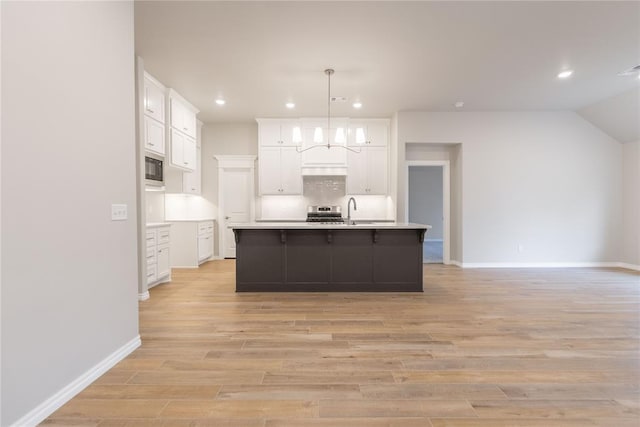 kitchen with decorative light fixtures, black microwave, white cabinetry, light hardwood / wood-style floors, and a center island with sink