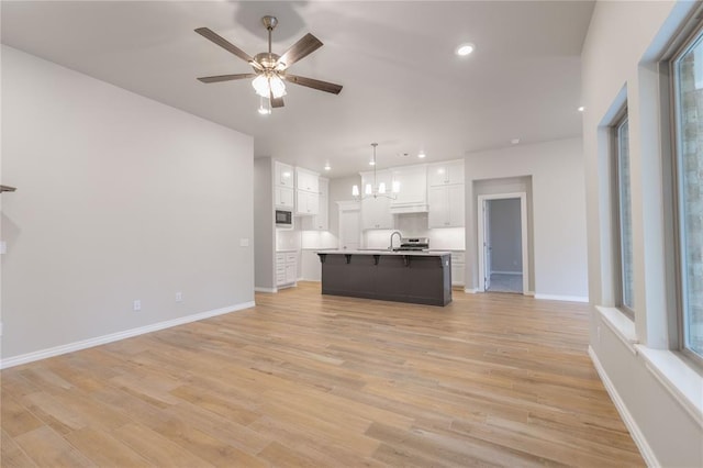 unfurnished living room with sink, ceiling fan with notable chandelier, and light wood-type flooring