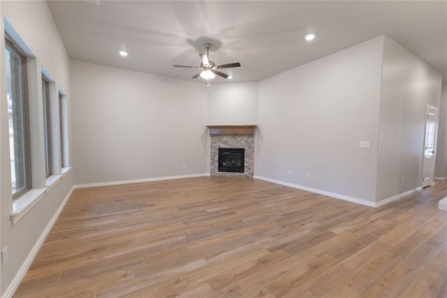 unfurnished living room featuring ceiling fan, a stone fireplace, and light wood-type flooring