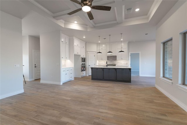 kitchen with appliances with stainless steel finishes, an island with sink, light wood-type flooring, pendant lighting, and white cabinetry