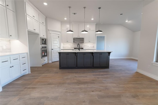 kitchen with white cabinets, hanging light fixtures, a kitchen island with sink, and appliances with stainless steel finishes