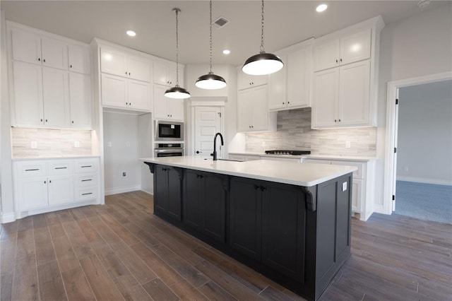 kitchen with sink, white cabinets, built in microwave, and an island with sink