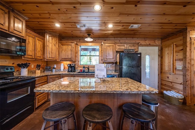 kitchen with a center island, light stone counters, wooden walls, and black appliances