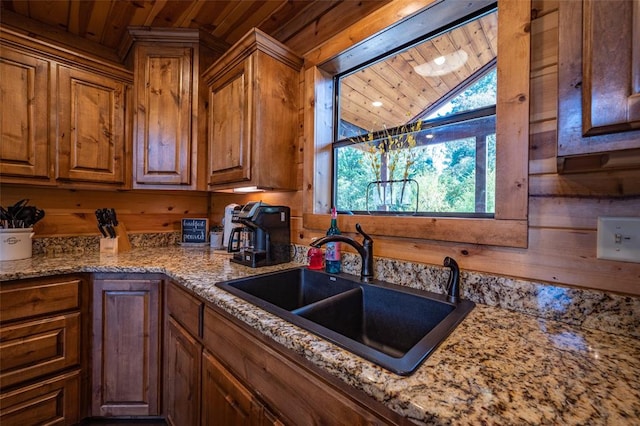 kitchen with light stone counters, wood ceiling, wooden walls, and sink