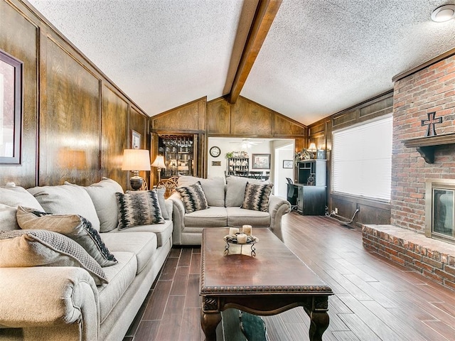 living room featuring a brick fireplace, a textured ceiling, dark wood-type flooring, lofted ceiling with beams, and wood walls