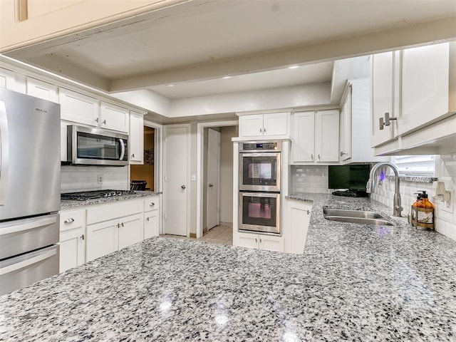 kitchen with backsplash, sink, light stone counters, white cabinetry, and stainless steel appliances