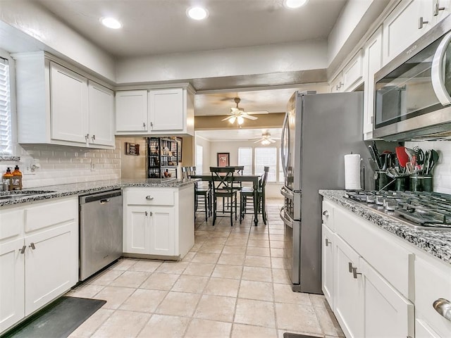 kitchen with kitchen peninsula, appliances with stainless steel finishes, tasteful backsplash, and white cabinetry