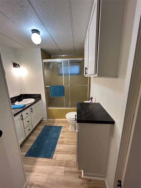 full bathroom featuring combined bath / shower with glass door, vanity, a textured ceiling, hardwood / wood-style floors, and toilet