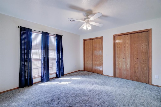 unfurnished bedroom with two closets, ceiling fan, and light colored carpet