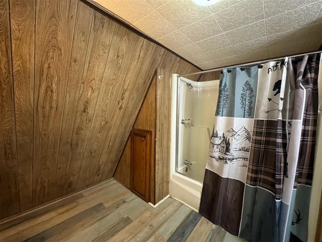 bathroom with vaulted ceiling, wood-type flooring, wooden walls, and shower / tub combo with curtain