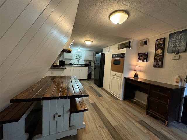 kitchen with sink, white cabinets, black appliances, and light wood-type flooring