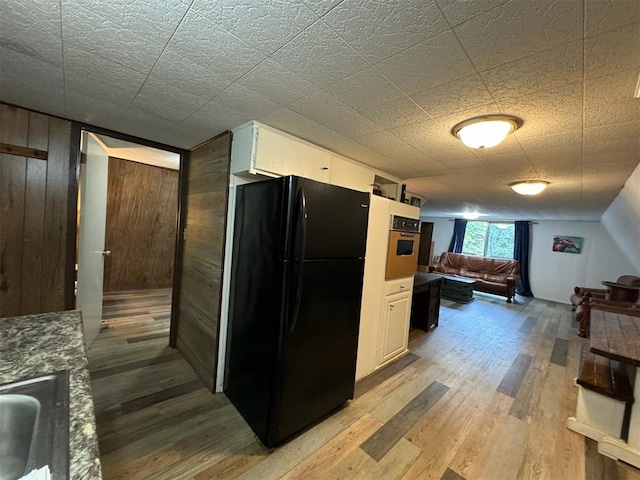 kitchen with light wood-type flooring, white cabinetry, black fridge, and wood walls