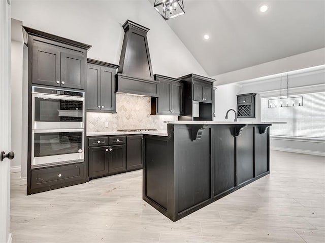 kitchen featuring decorative light fixtures, custom exhaust hood, stainless steel appliances, and a center island with sink