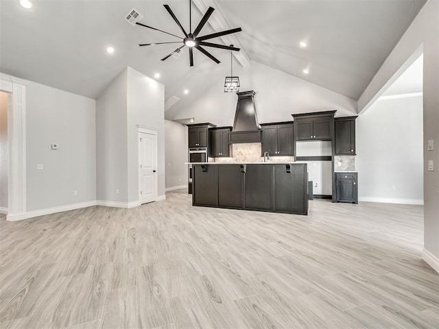 kitchen featuring stainless steel oven, light hardwood / wood-style flooring, an island with sink, custom range hood, and backsplash