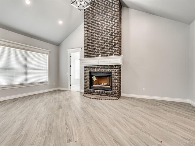 unfurnished living room with a brick fireplace, high vaulted ceiling, and light wood-type flooring