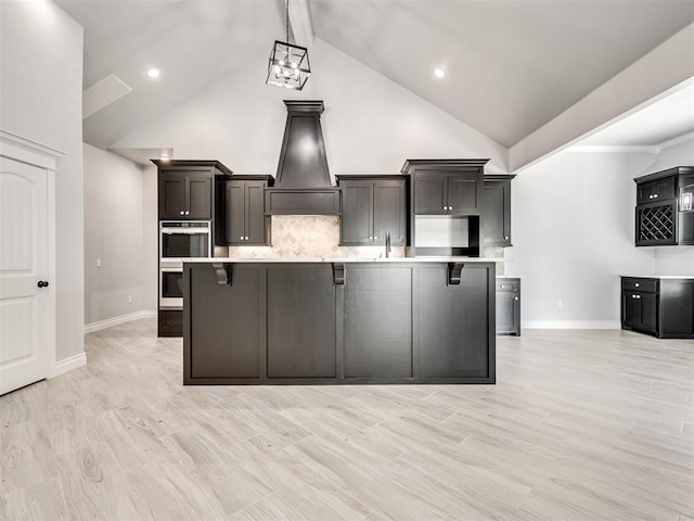 kitchen with an island with sink, high vaulted ceiling, a breakfast bar area, and light hardwood / wood-style floors