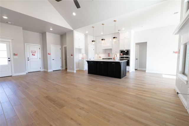 kitchen with hanging light fixtures, a kitchen island with sink, white cabinets, high vaulted ceiling, and stainless steel appliances