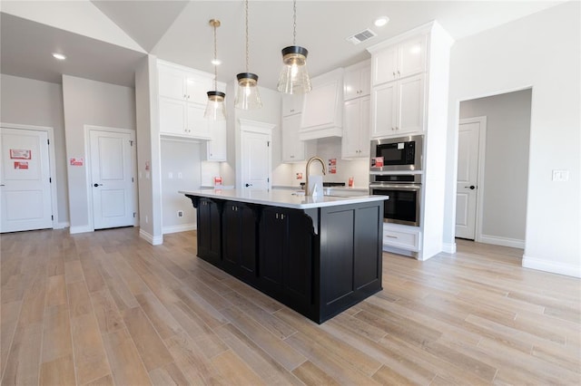 kitchen with built in microwave, decorative light fixtures, white cabinetry, oven, and a center island with sink