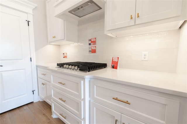 kitchen with stainless steel gas stovetop, light wood-type flooring, white cabinetry, wall chimney range hood, and decorative backsplash