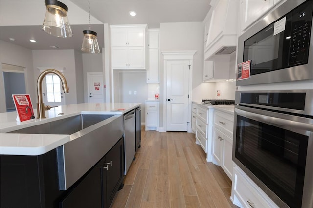 kitchen with light hardwood / wood-style floors, white cabinetry, a kitchen island with sink, pendant lighting, and stainless steel appliances