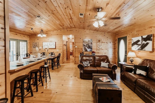 living room with light wood-type flooring, wood ceiling, ceiling fan with notable chandelier, vaulted ceiling, and wooden walls