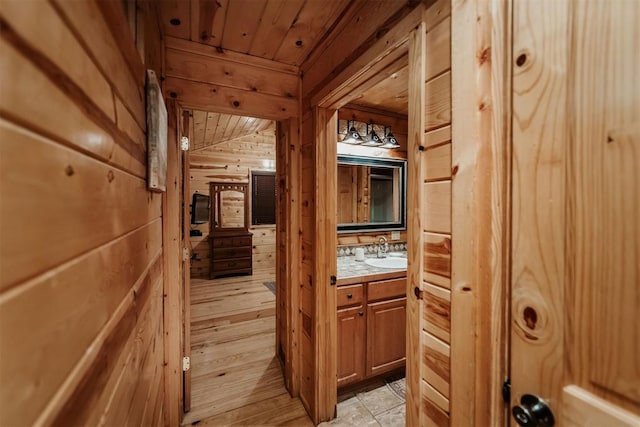 hall featuring sink, wood walls, light hardwood / wood-style floors, lofted ceiling, and wood ceiling